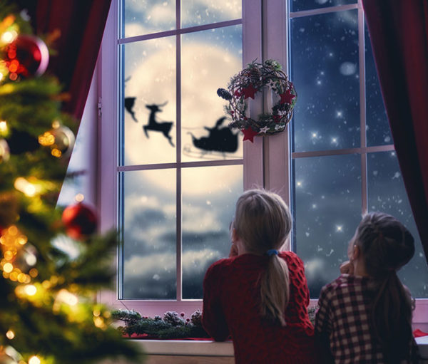 children looking at window at Santa and reindeer against a full moon