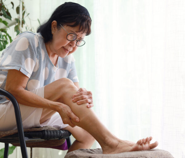 Portrait of a distraught senior Asian woman holding sore leg muscle. Health care and medical concept.