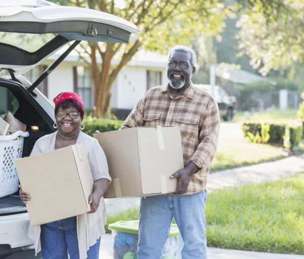 A senior African-American couple relocating, moving to a new home. They are excited, unloading boxes from their car. They are in their 70s, downsizing in retirement.