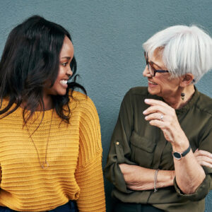 Shot of two cheerful businesswomen having a discussion while standing against a wall outdoors