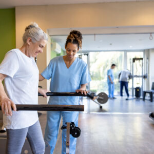 Senior woman in physical therapy walking on the bars with the help of her therapist - orthopedic medicine concepts
